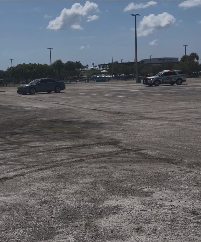 Nearly empty parking lot with a few scattered cars, utility poles, and clear sky with white clouds